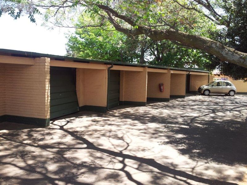 A row of open-style brick garages with a damaged door, situated under mature trees with an asphalt driveway.