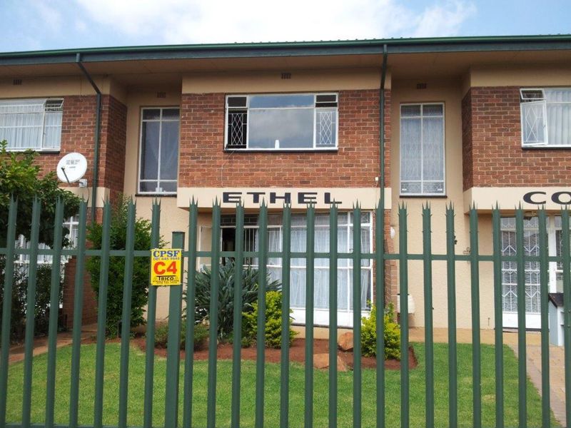 Front elevation of a brick townhouse complex featuring security fencing and metal security bars on windows.