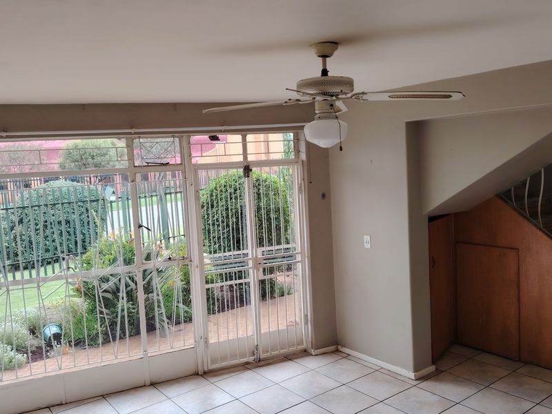 An open-plan living area featuring tiled floors, a ceiling fan, and direct access to the garden through a secure metal-framed door.