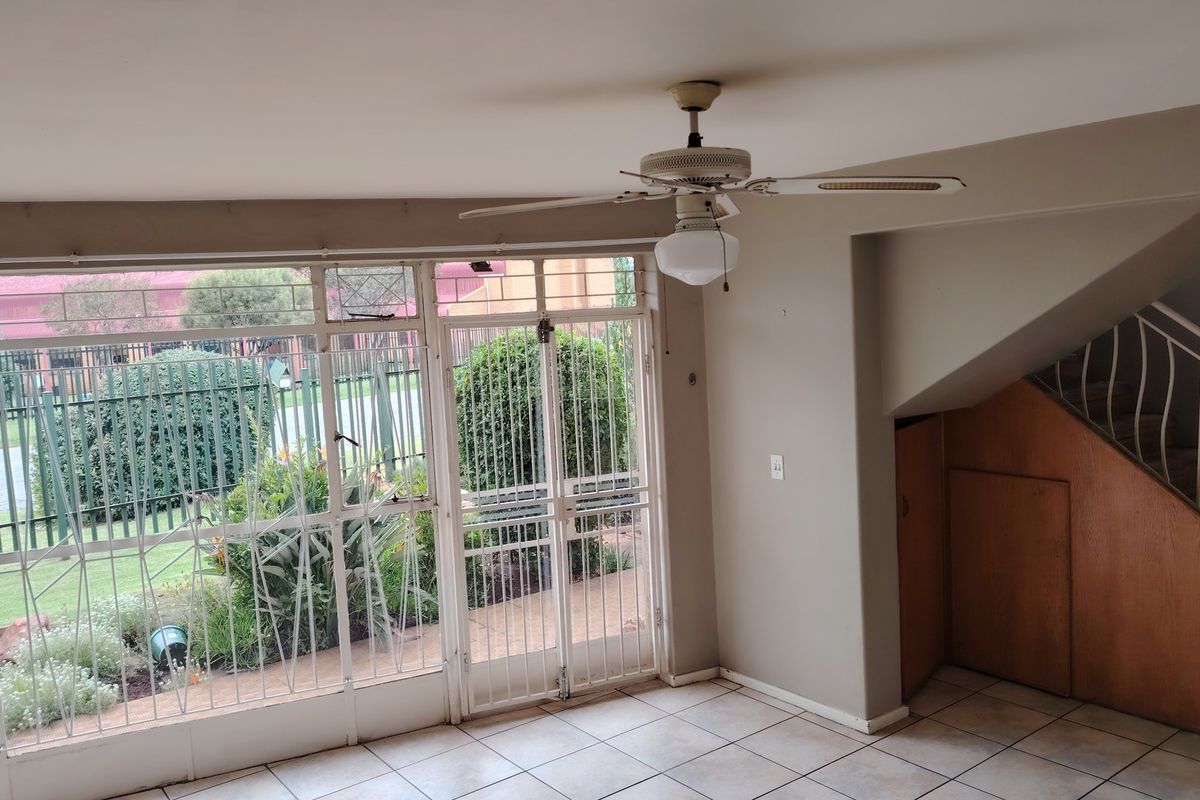 An open-plan living area featuring tiled floors, a ceiling fan, and direct access to the garden through a secure metal-framed door.
