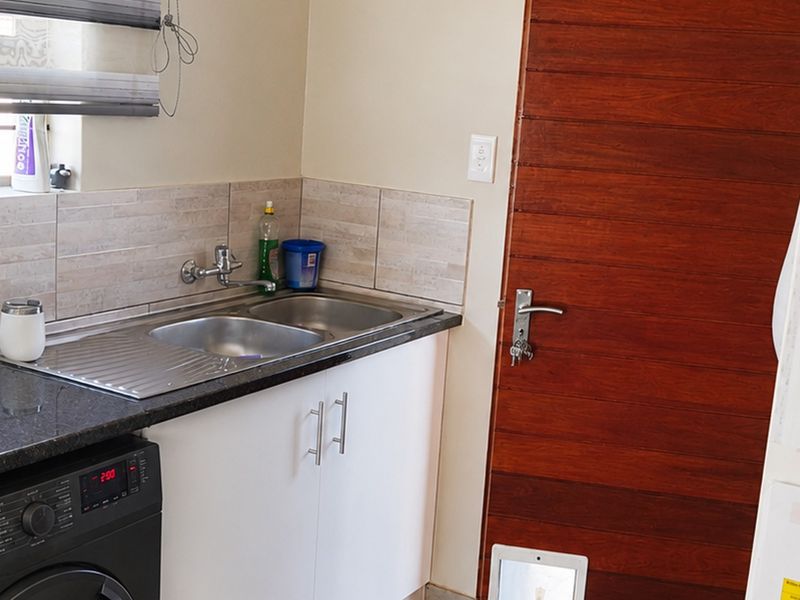 A functional scullery area featuring a double stainless steel sink, granite countertops, built-in cabinetry, and a timber door with an integrated pet flap.