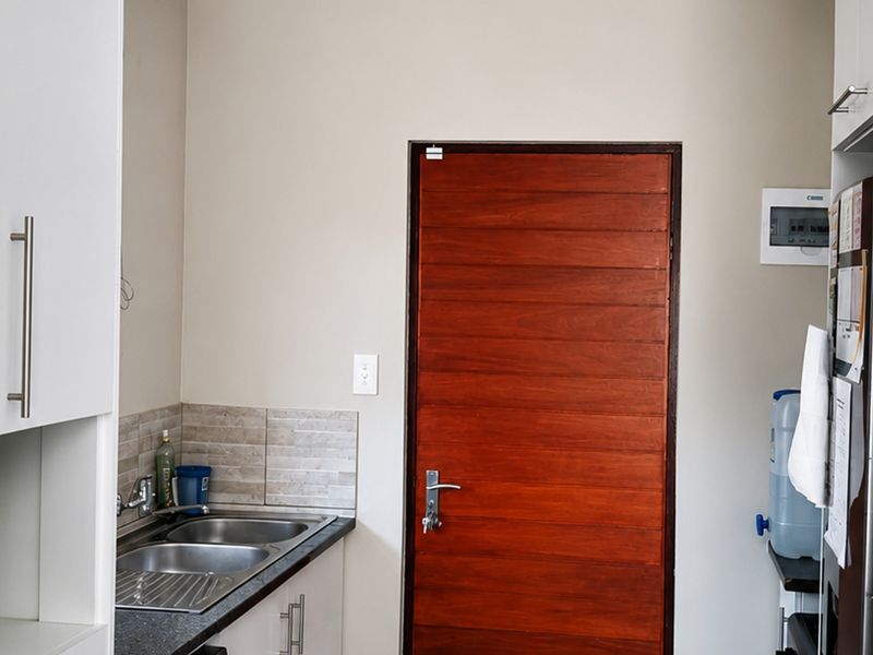 A functional scullery area featuring built-in cabinetry, a double bowl stainless steel sink, and a tiled splashback, providing convenient additional workspace.
