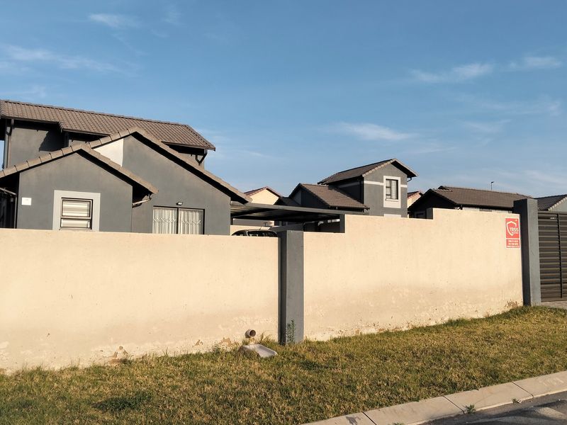 Front view of a residential property featuring a perimeter wall, tiled roof, and a secure gated entrance with a paved driveway.