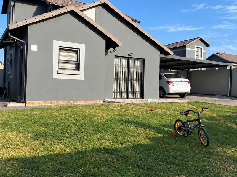 Rear view of a modern grey house featuring a paved driveway, attached carport, and a private garden area with boundary walls.