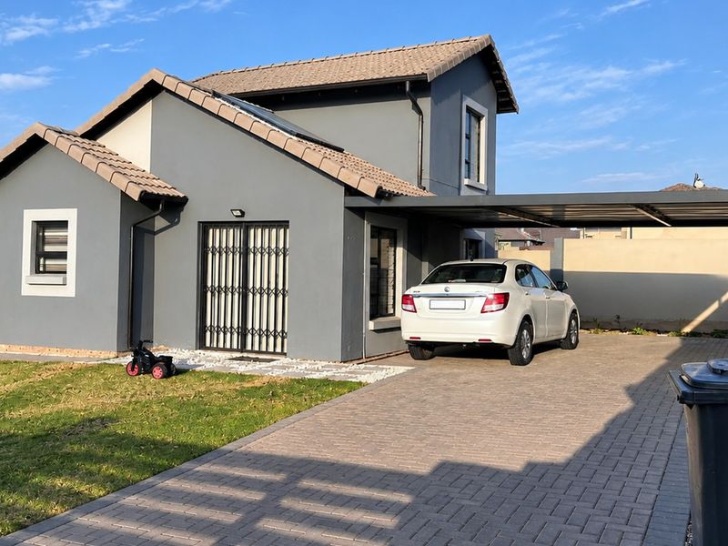 A modern single-story house featuring a grey facade, tiled roof, paved driveway, and a covered carport, set within a secure residential property.