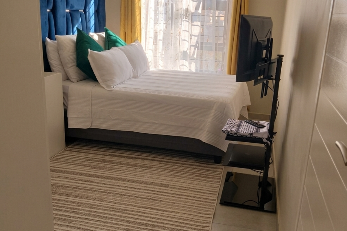 A well-lit bedroom featuring tiled flooring, a built-in cupboard, and a window with curtain rod, providing a comfortable and functional living space.
