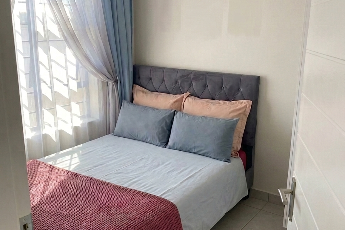 A compact bedroom featuring neutral tiled flooring, a window with security bars, and a clean, modern interior finish.