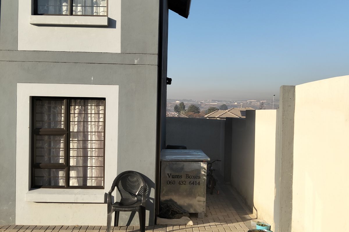 A side view of the property featuring a paved patio area, a small garden bed, and boundary walling with security bars on the windows.