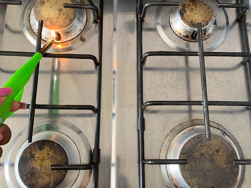 A close-up view of a four-burner stainless steel gas hob showing significant wear and carbon buildup on the burner caps.