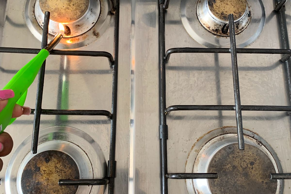 A close-up view of a four-burner stainless steel gas hob showing significant wear and carbon buildup on the burner caps.