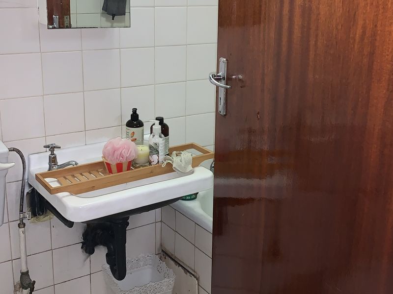 A compact bathroom featuring a wall-mounted basin, tiled finishes, and a bathtub, requiring some maintenance to the lower wall tiling and plumbing fixtures.