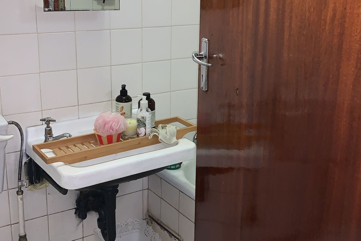 A compact bathroom featuring a wall-mounted basin, tiled finishes, and a bathtub, requiring some maintenance to the lower wall tiling and plumbing fixtures.