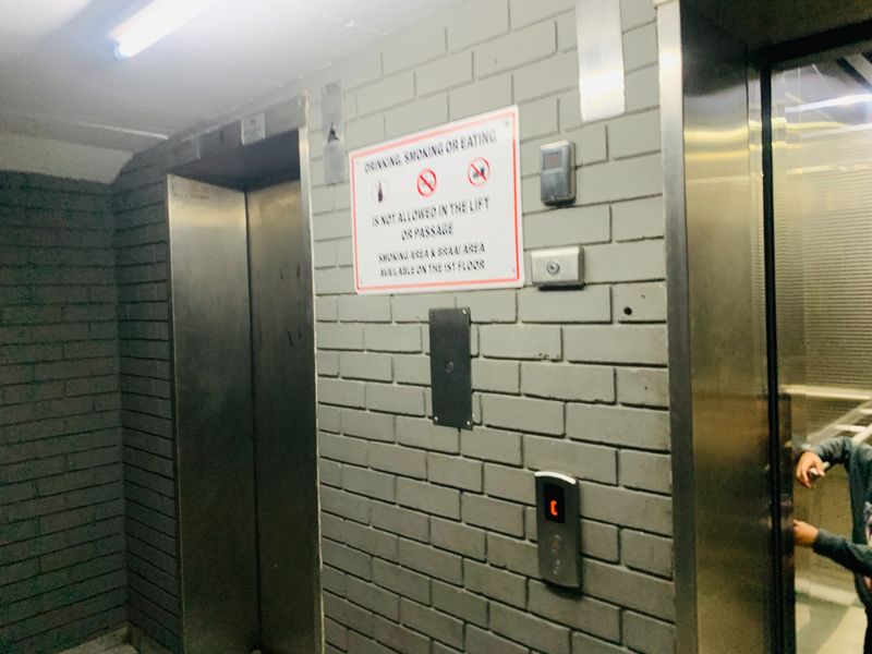 A communal apartment building hallway featuring an elevator and brick wall finish with building signage.