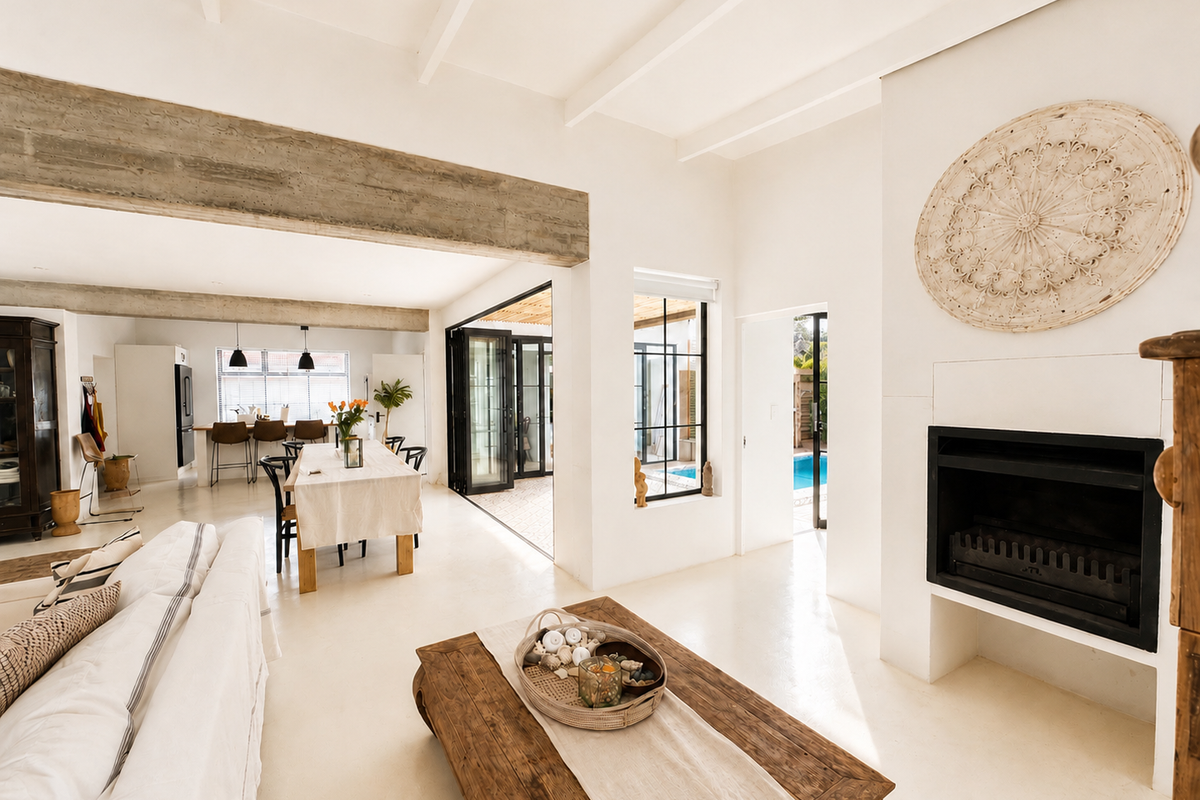 Spacious open-plan living area featuring a built-in fireplace, exposed concrete beams, polished concrete flooring, and seamless flow to the outdoor patio and pool area.