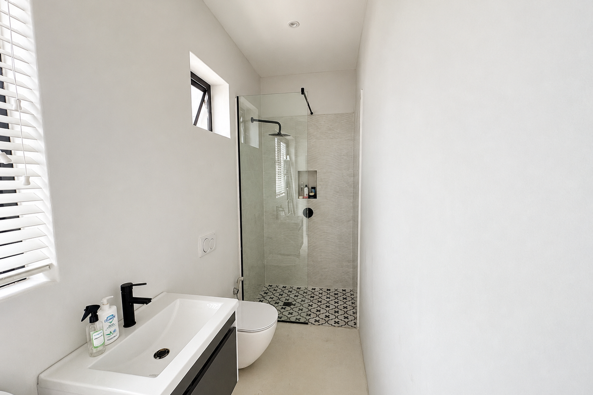 Modern bathroom featuring a sleek vanity, wall-mounted toilet, and a walk-in shower with patterned floor tiles and a rainfall showerhead.