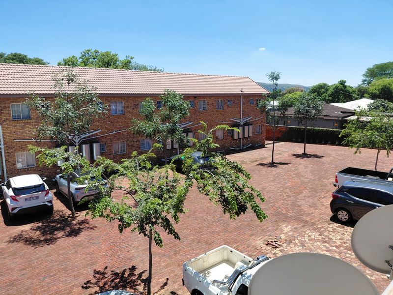 An elevated view of the rear exterior of the apartment complex, featuring a brick facade, tiled roof, and a paved parking courtyard.