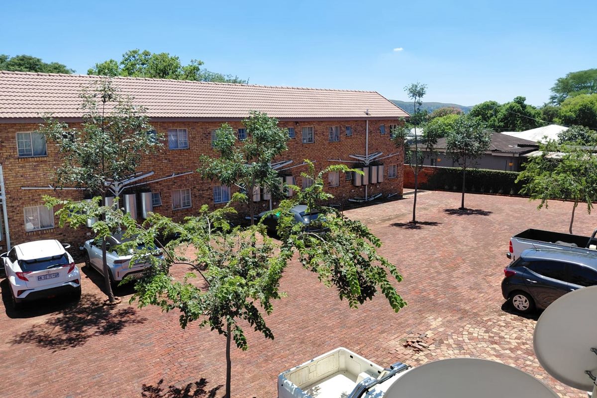An elevated view of the rear exterior of the apartment complex, featuring a brick facade, tiled roof, and a paved parking courtyard.