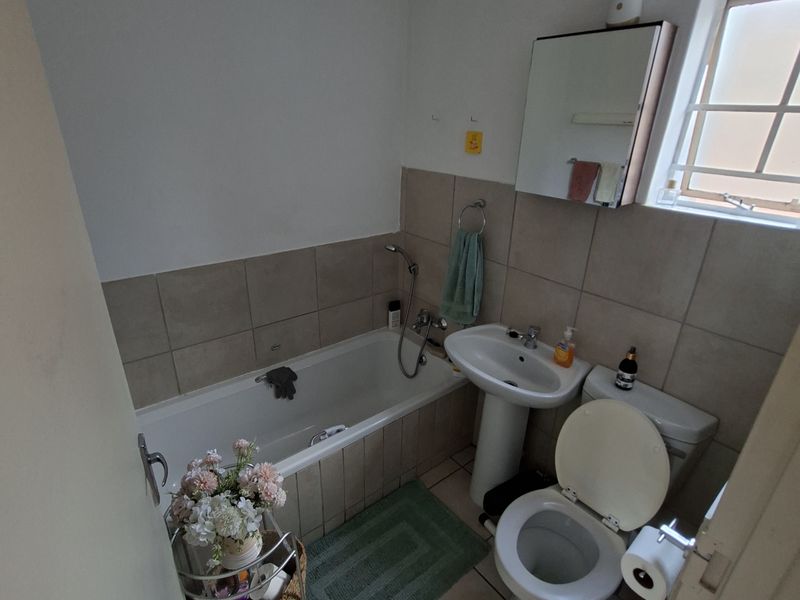 A functional bathroom featuring a bathtub, pedestal basin, and toilet with neutral wall and floor tiling.