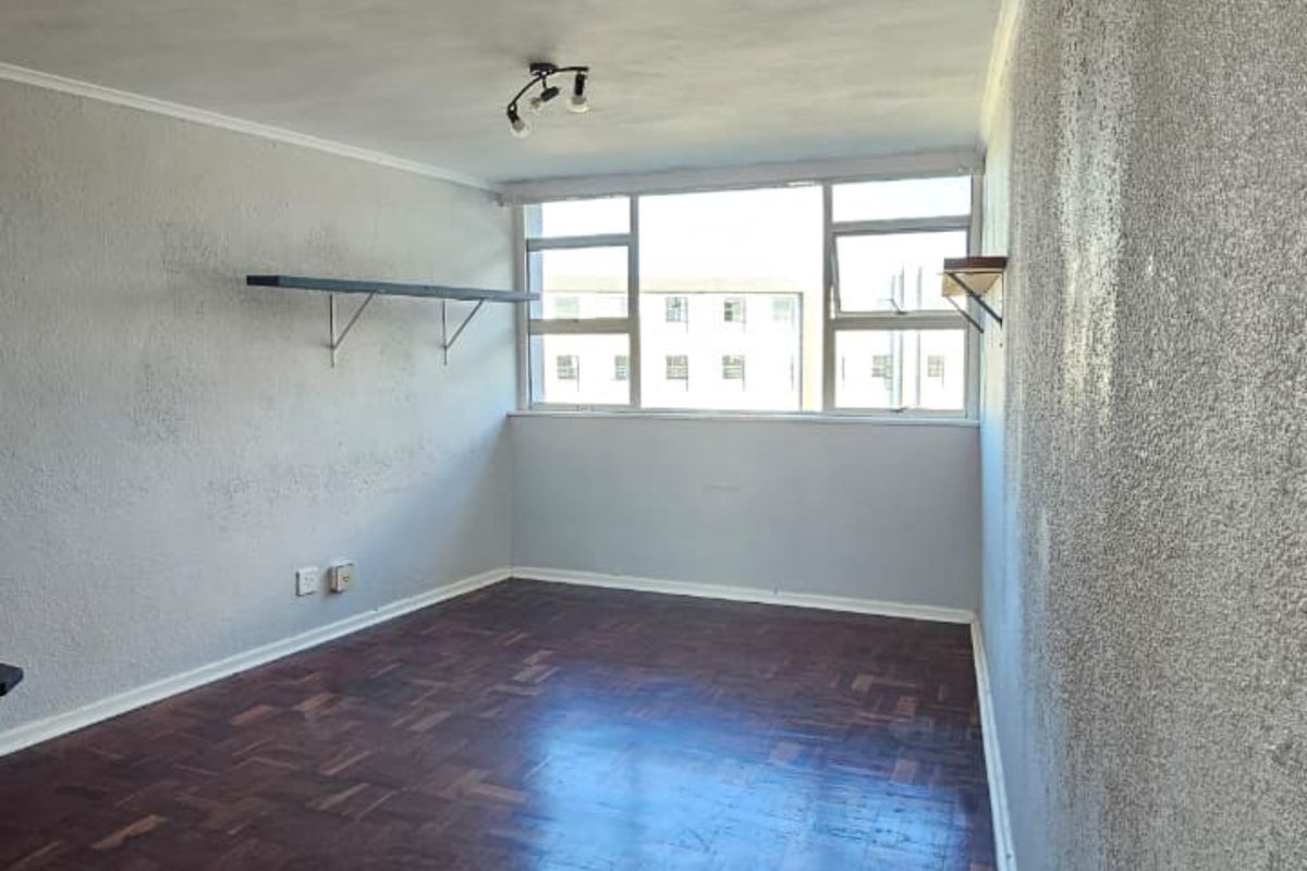 An empty bedroom featuring classic parquet wood flooring, textured walls, and large windows providing natural light.