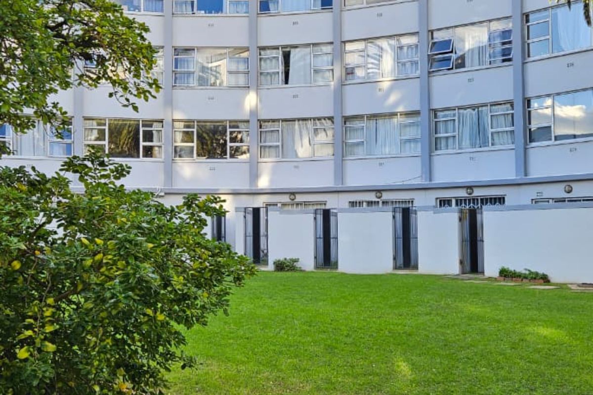 A view of the rear exterior facade of a multi-story apartment building featuring a shared lawn and garden area.