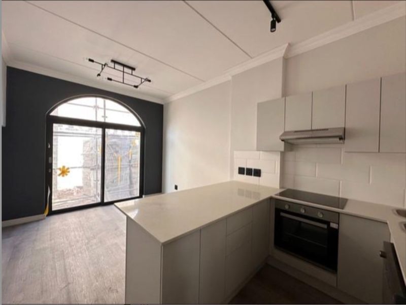 Modern open-plan kitchen and living area featuring sleek cabinetry, stone countertops, integrated appliances, and a large arched sliding door leading to an outdoor space.