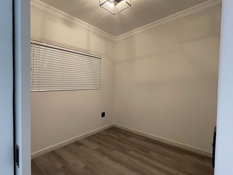 A clean, empty bedroom featuring modern laminate flooring, crown molding, and a contemporary flush mount ceiling light fixture.