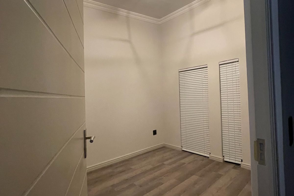 A clean, empty bedroom featuring modern laminate flooring, crown molding, and dual windows with fitted venetian blinds.