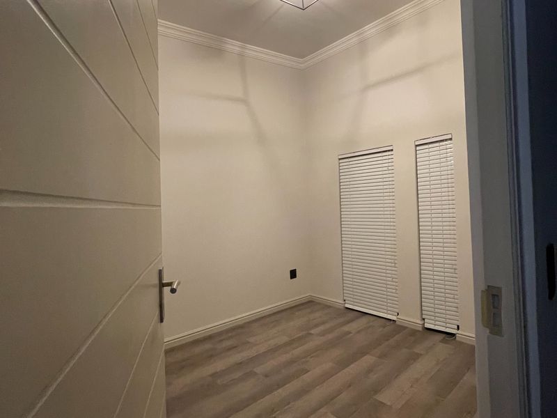 A clean, empty bedroom featuring modern laminate flooring, crown molding, and dual windows with fitted venetian blinds.