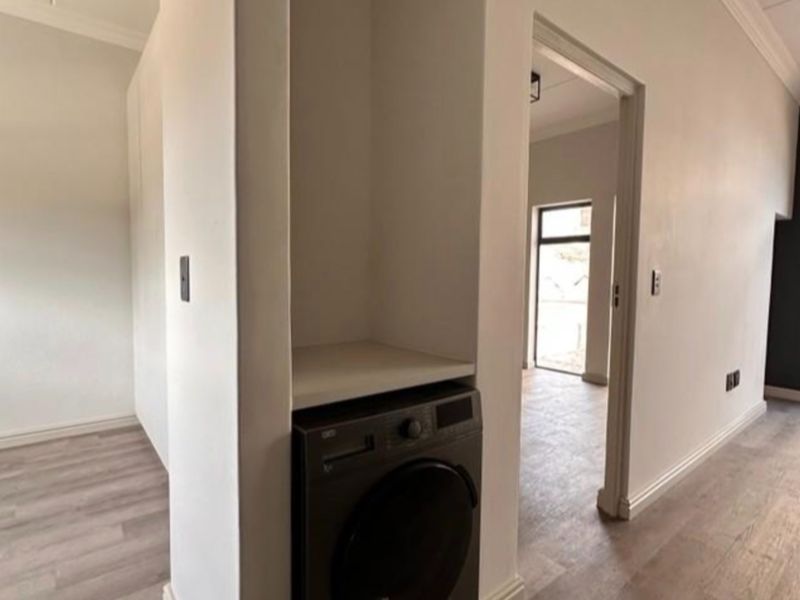 A dedicated laundry nook featuring built-in shelving and space for a washing machine, set within a clean, neutral interior space.