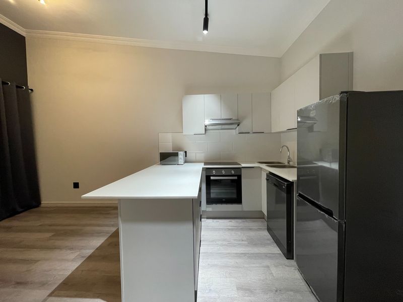 Modern kitchen featuring white cabinetry, a central island, built-in oven, hob, extractor fan, and light-toned laminate flooring in an open-plan layout.