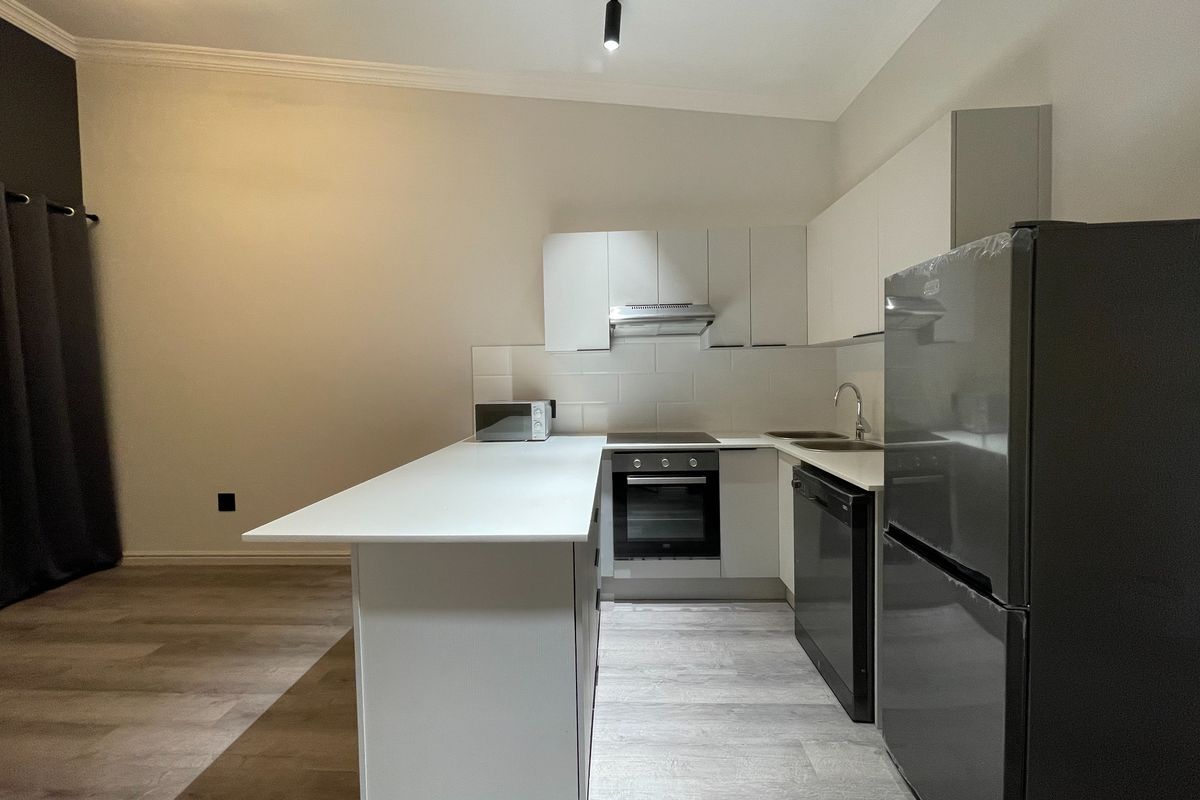 Modern kitchen featuring white cabinetry, a central island, built-in oven, hob, extractor fan, and light-toned laminate flooring in an open-plan layout.