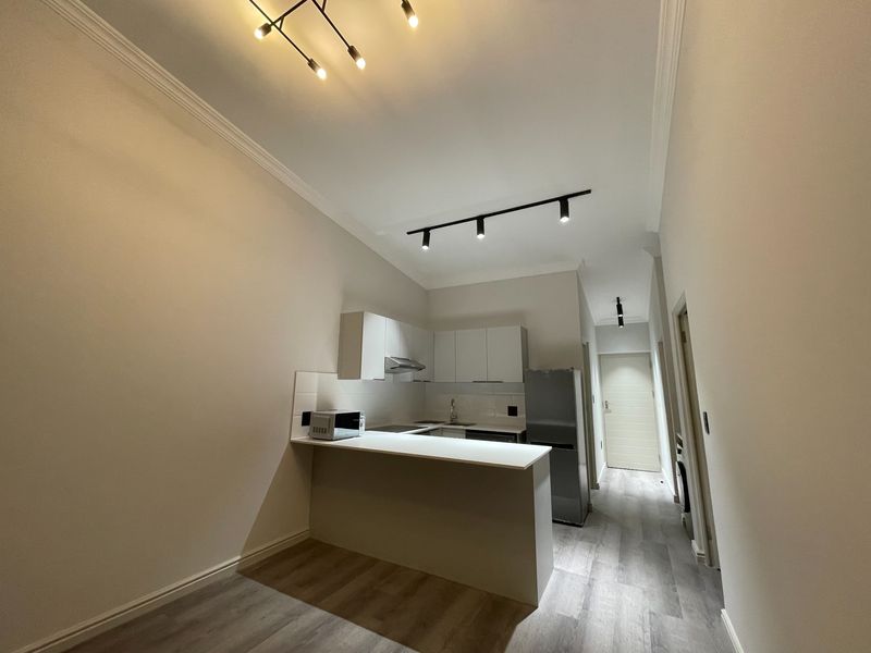 Modern kitchen featuring white cabinetry, a breakfast bar, track lighting, and light-toned laminate flooring in an open-plan layout.