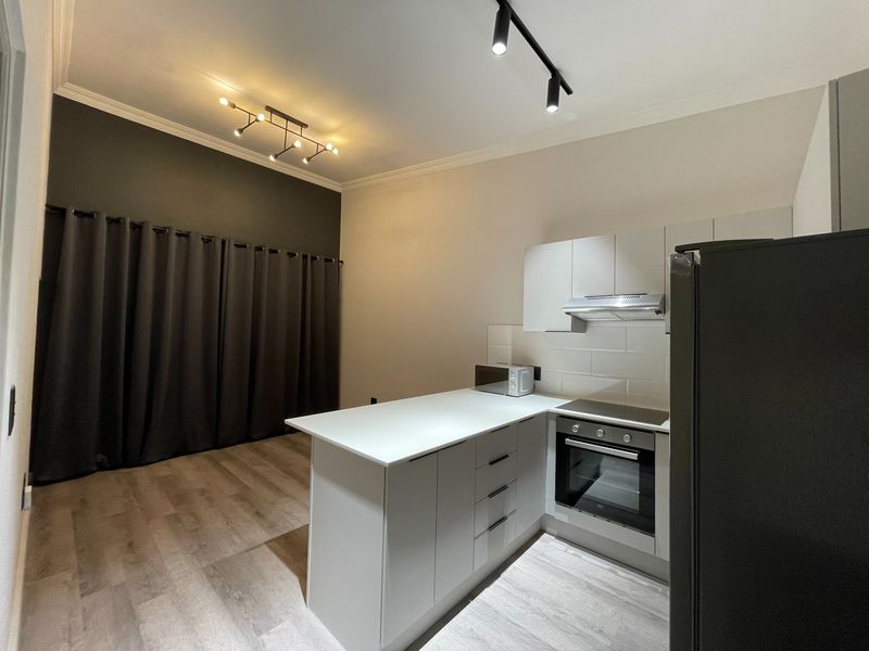 Modern open-plan kitchen and living area featuring sleek cabinetry, built-in appliances, subway tile backsplash, and contemporary track lighting.