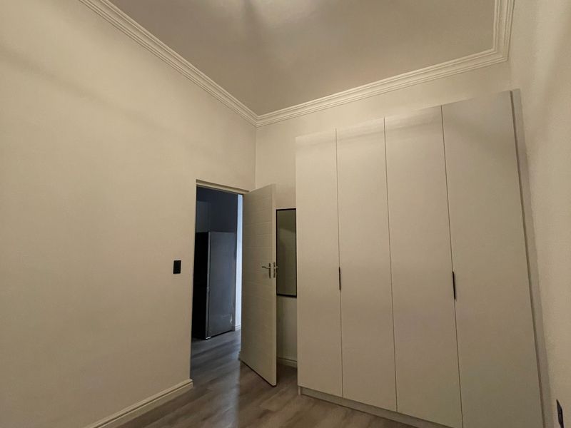 A clean, empty bedroom featuring modern laminate flooring, built-in wardrobes, and decorative ceiling cornicing.