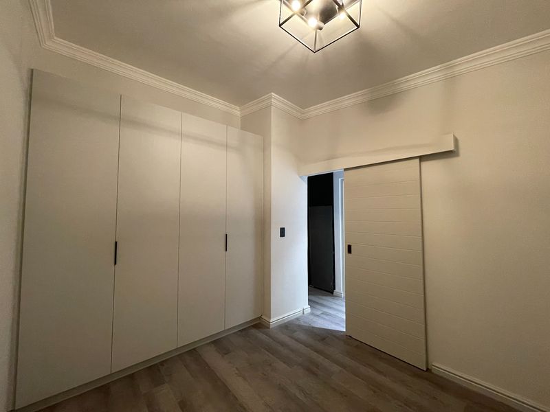 A clean, modern bedroom featuring built-in floor-to-ceiling cupboards, a stylish sliding barn door, and neutral laminate flooring with elegant crown molding.
