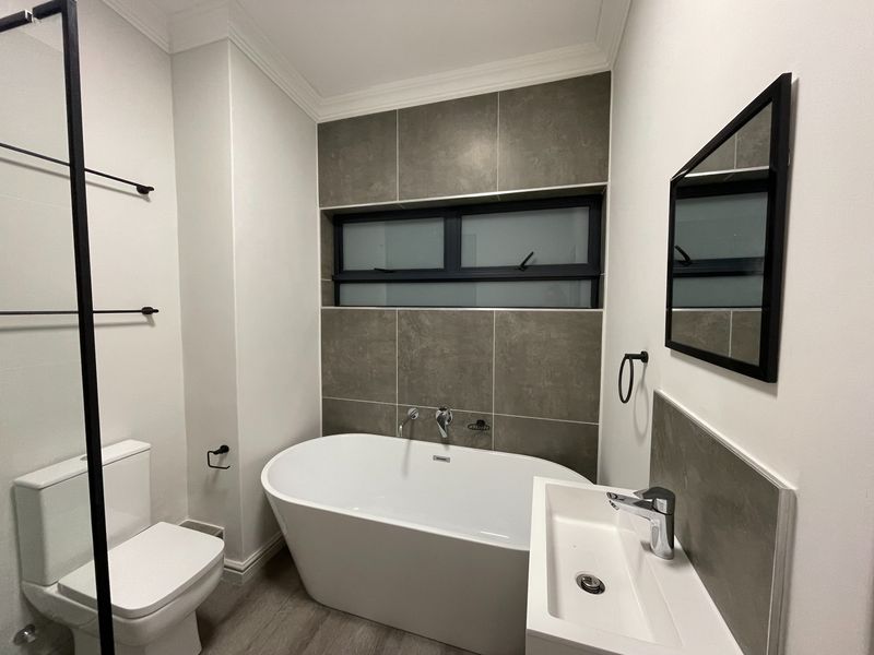 Modern bathroom featuring a sleek freestanding bathtub, wall-mounted basin, contemporary chrome fixtures, and stylish dark-toned tiled accents.