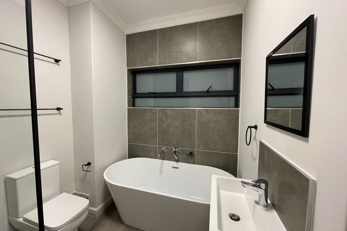 Modern bathroom featuring a sleek freestanding bathtub, wall-mounted basin, contemporary chrome fixtures, and stylish dark-toned tiled accents.