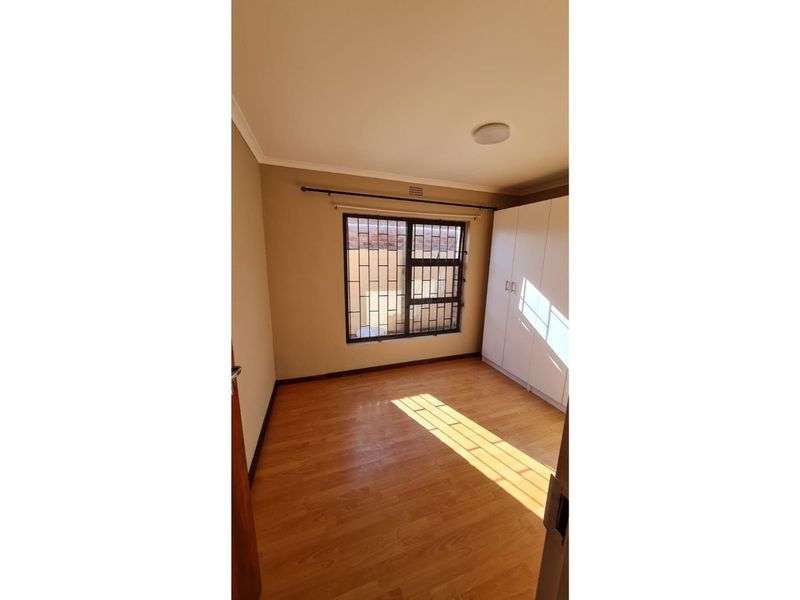 A bright, empty bedroom featuring laminate flooring, a built-in wardrobe, and a window fitted with security bars.