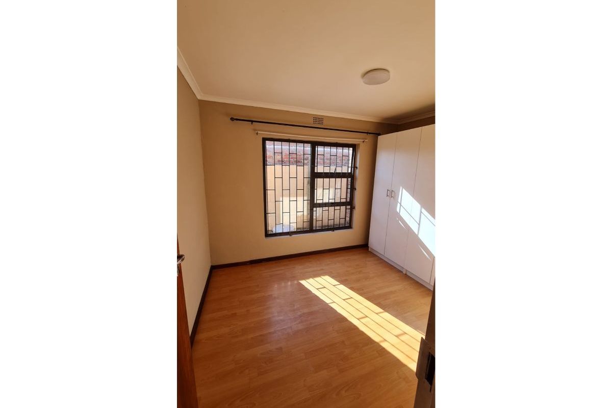 A bright, empty bedroom featuring laminate flooring, a built-in wardrobe, and a window fitted with security bars.