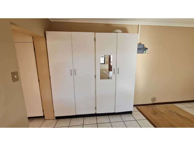 A bedroom featuring a large white built-in wardrobe, tiled flooring, and a wall-mounted electrical distribution board.