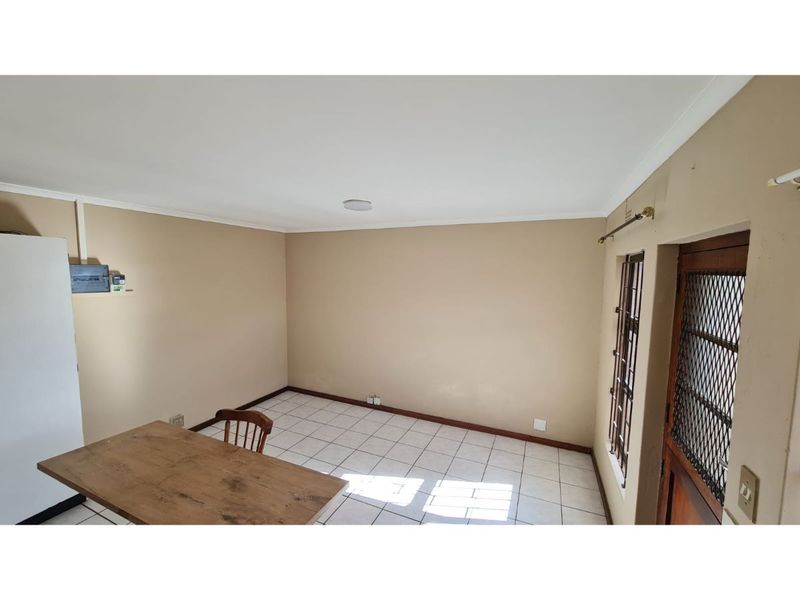 An empty living area featuring tiled flooring, neutral wall paint, and a secure entrance door with a metal security gate.