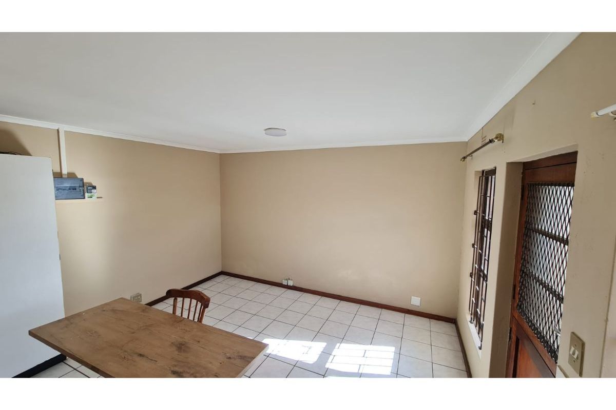An empty living area featuring tiled flooring, neutral wall paint, and a secure entrance door with a metal security gate.
