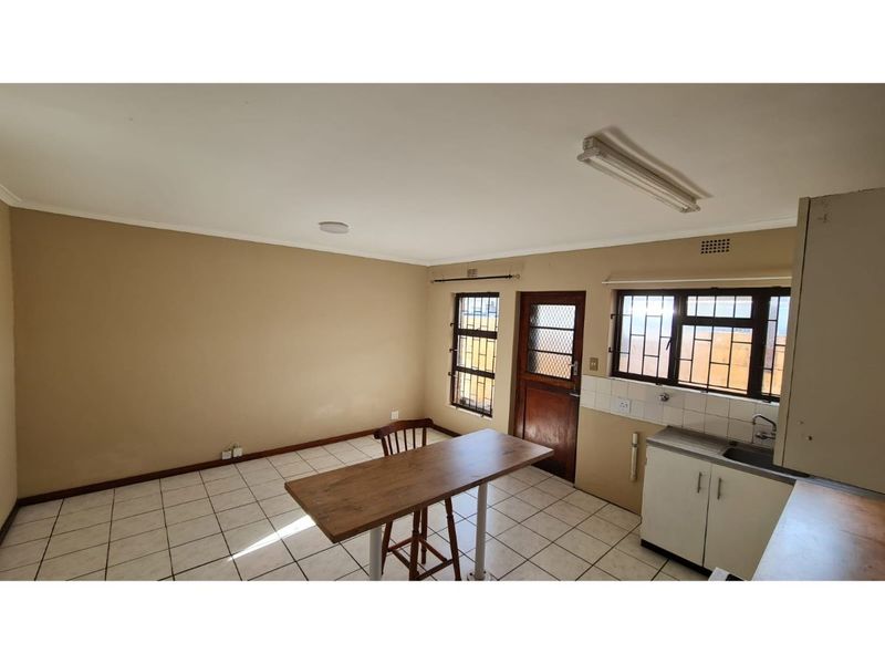 Open plan kitchen and living area featuring tiled flooring, basic cabinetry, and security gates on windows and doors.