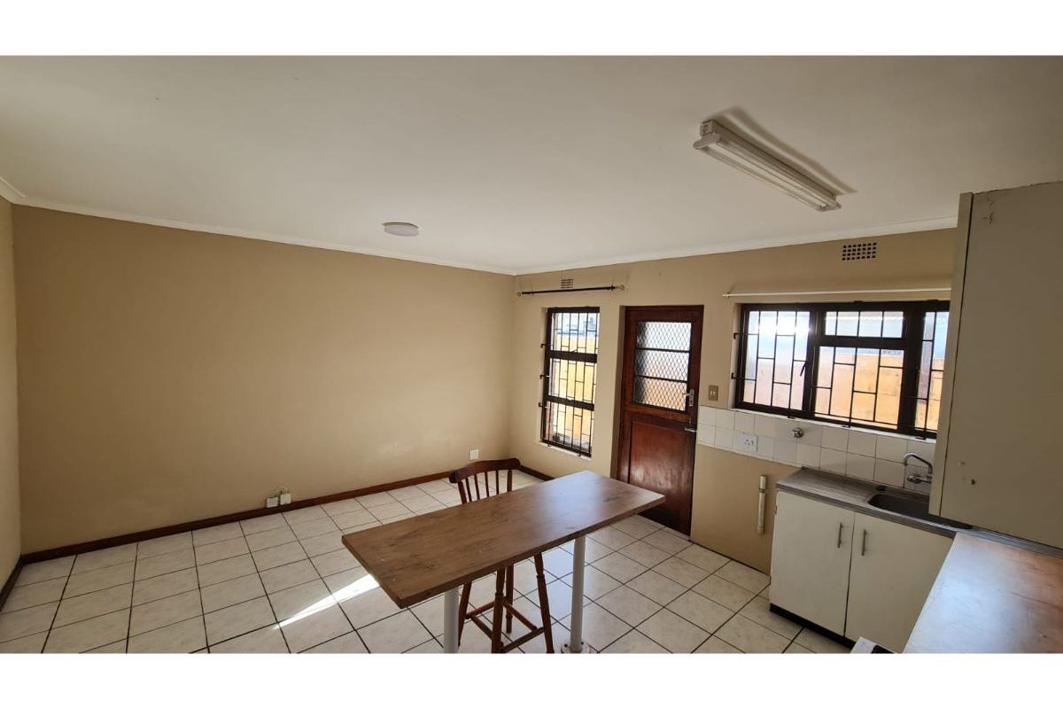 Open plan kitchen and living area featuring tiled flooring, basic cabinetry, and security gates on windows and doors.
