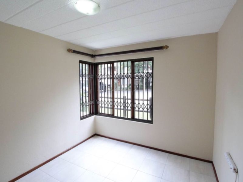 A vacant bedroom featuring neutral walls, tiled flooring, and security bars on the corner windows.