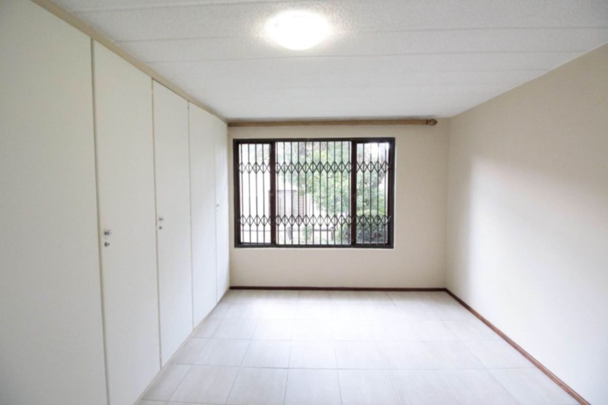 A bright, empty bedroom featuring built-in floor-to-ceiling cupboards and a window fitted with security bars.