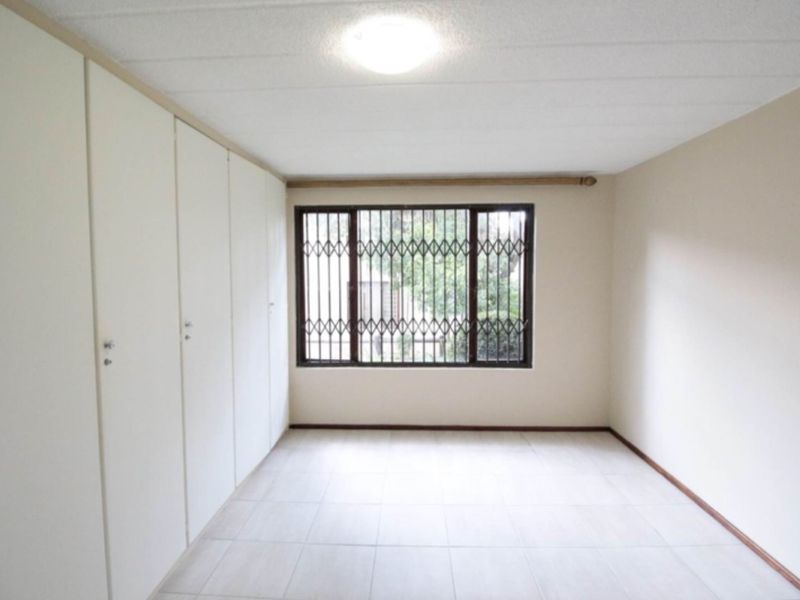 A bright, empty bedroom featuring built-in floor-to-ceiling cupboards and a window fitted with security bars.