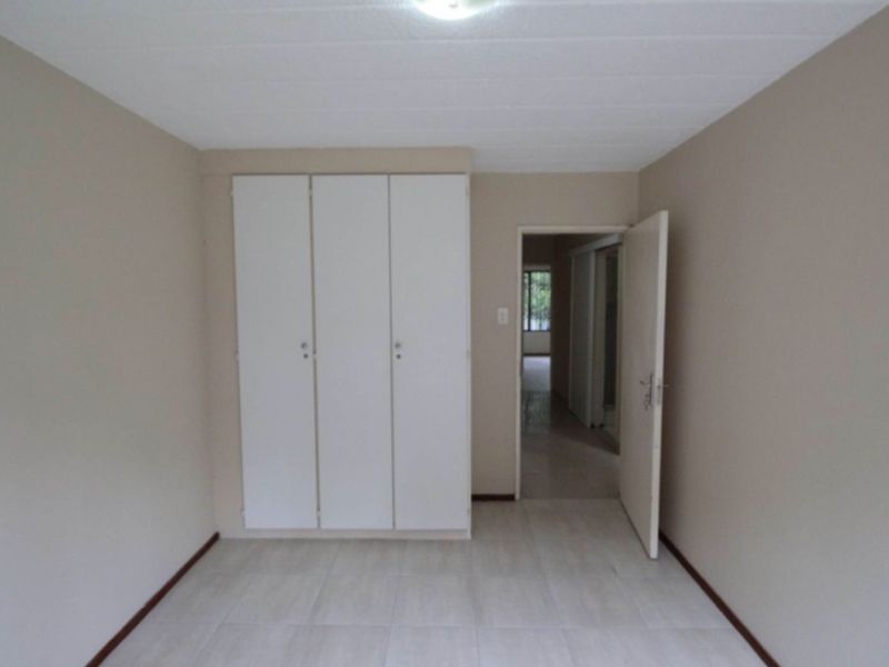 A clean, empty bedroom featuring neutral wall tones, tiled flooring, and built-in white cabinetry.