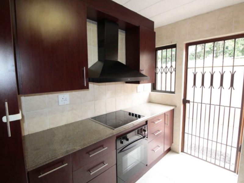 A functional kitchen featuring dark wood cabinetry, stone countertops, a built-in electric hob, oven, and extractor fan, with direct access to the exterior.