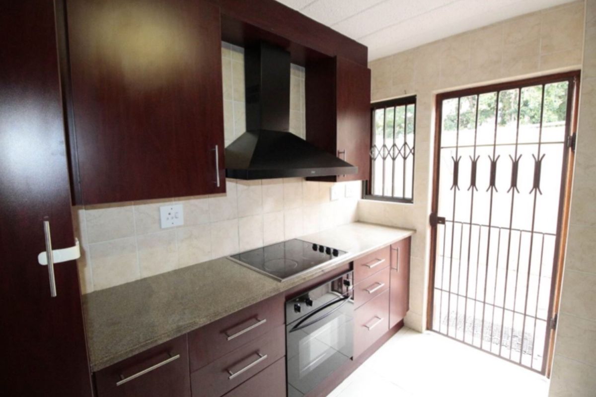 A functional kitchen featuring dark wood cabinetry, stone countertops, a built-in electric hob, oven, and extractor fan, with direct access to the exterior.